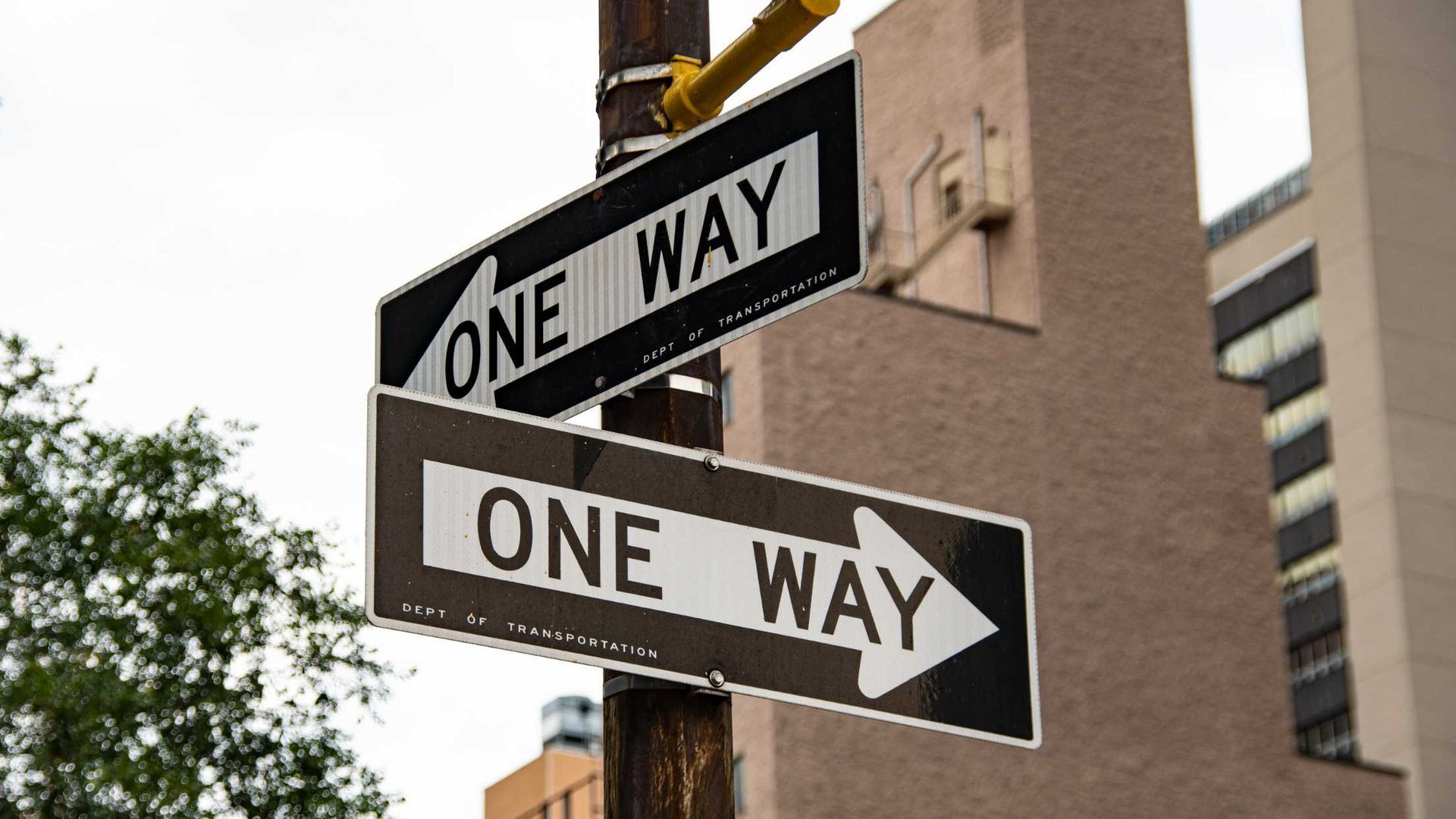 Two one way street signs are on a pole in front of a building.