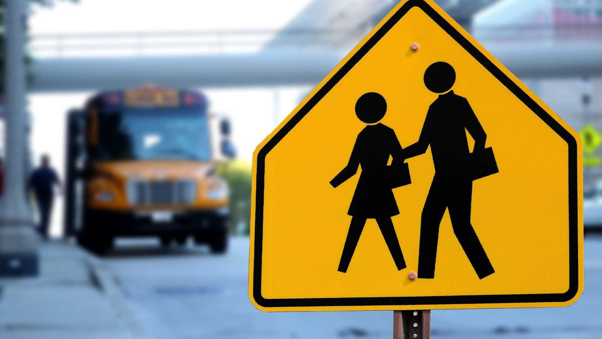 A yellow school crossing sign with a school bus in the background.