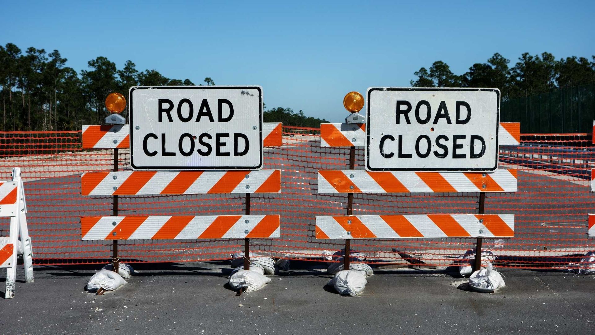 Two orange and white road closed signs on the side of a road