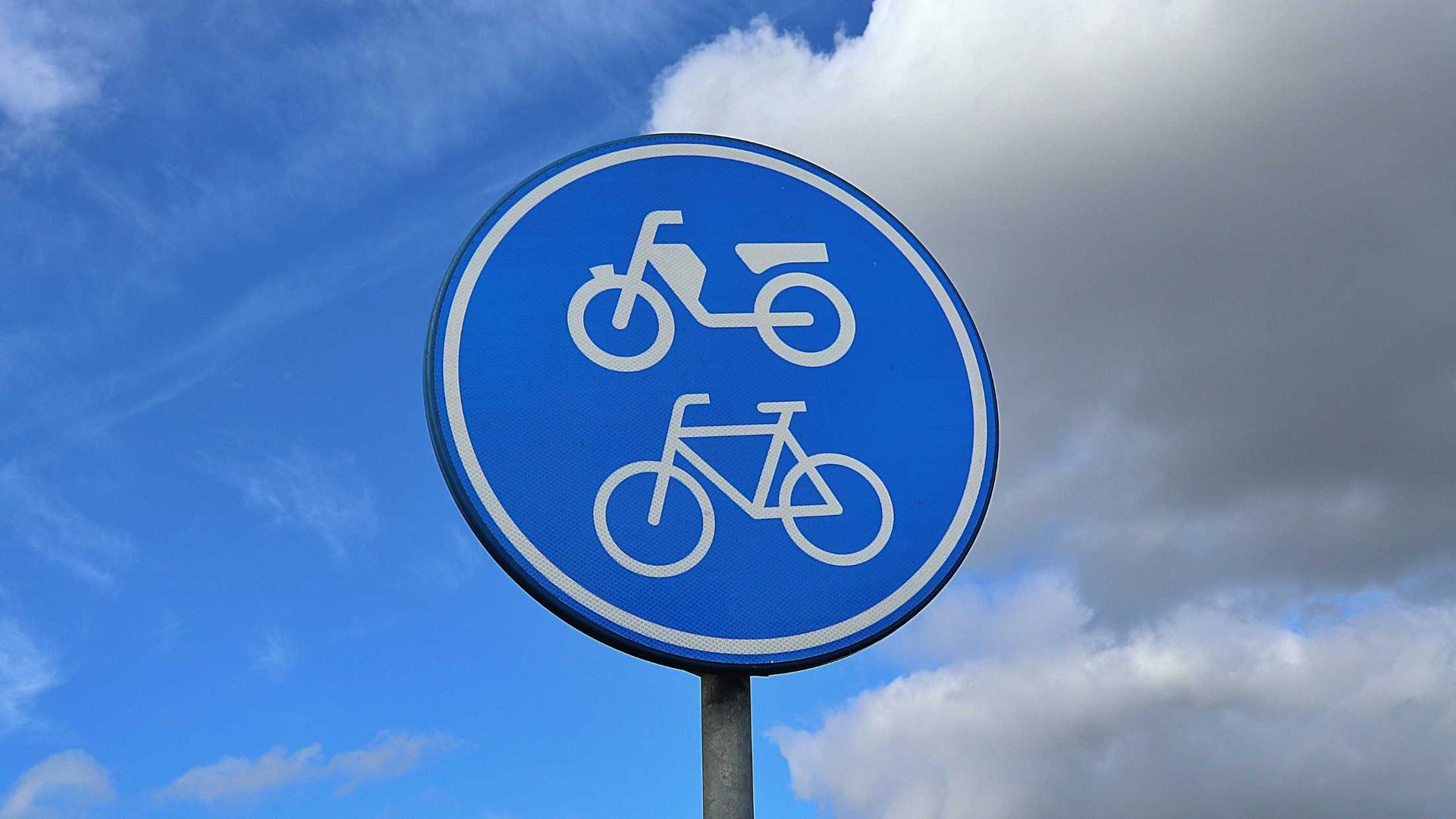 A blue and white bicycle sign against a cloudy blue sky