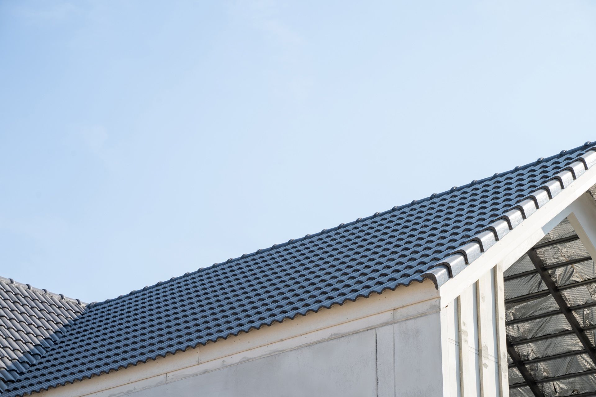 Blue sky over a dark gray tiled roof on a white building.