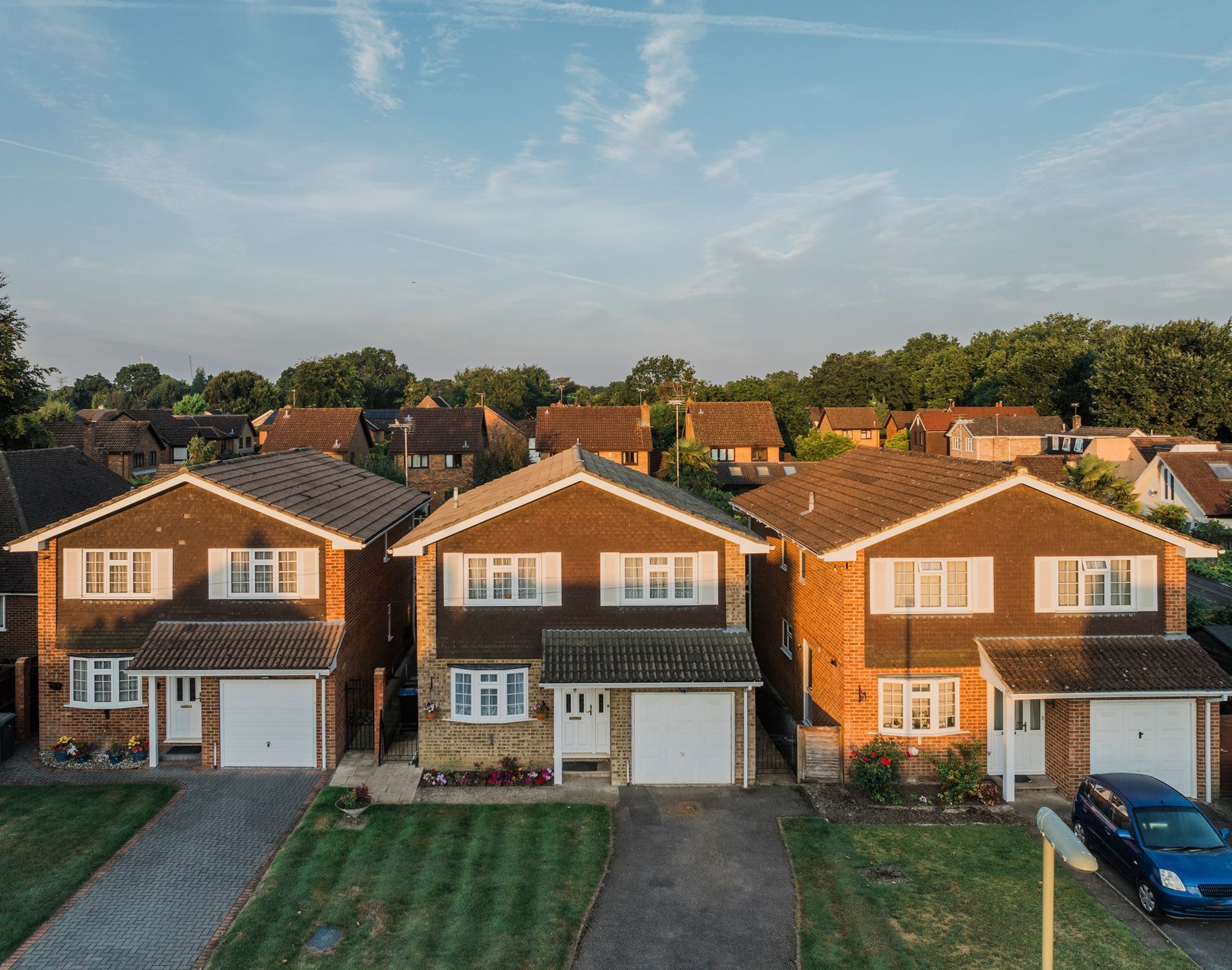 Three suburban houses with beige and brown exteriors and white garage doors, under a blue sky.