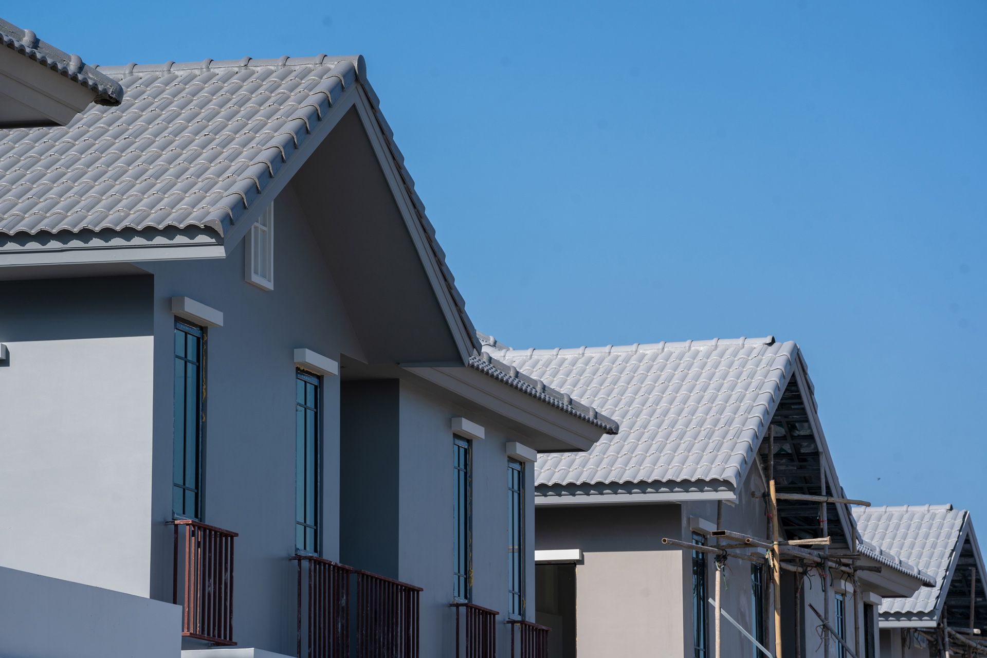 Row of modern gray houses with light gray tiled roofs against a clear blue sky.