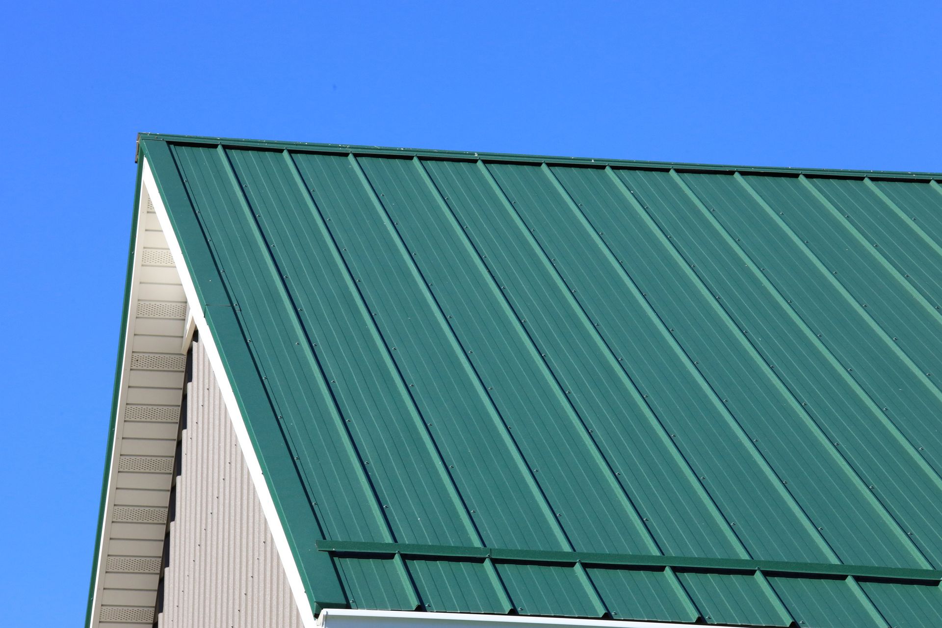 Green metal roof on a building against a clear blue sky.