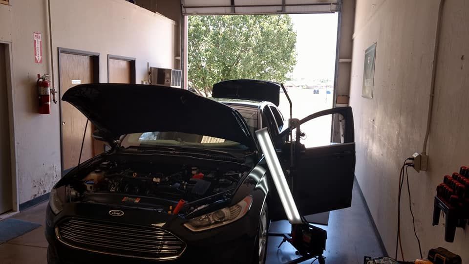 A black car with the hood up is sitting in a garage.