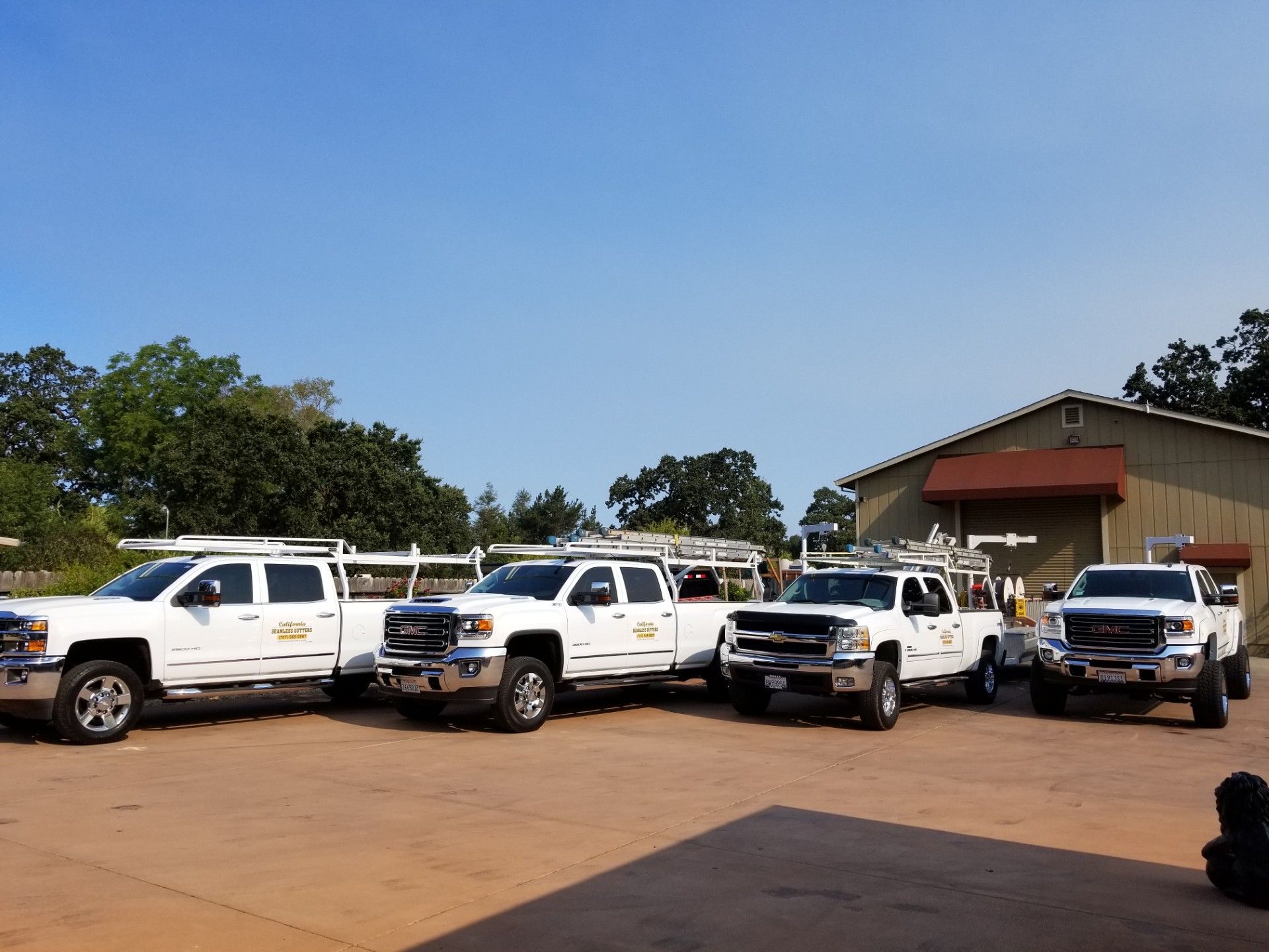Several white utility trucks parked in a lot beside a building under a clear blue sky.