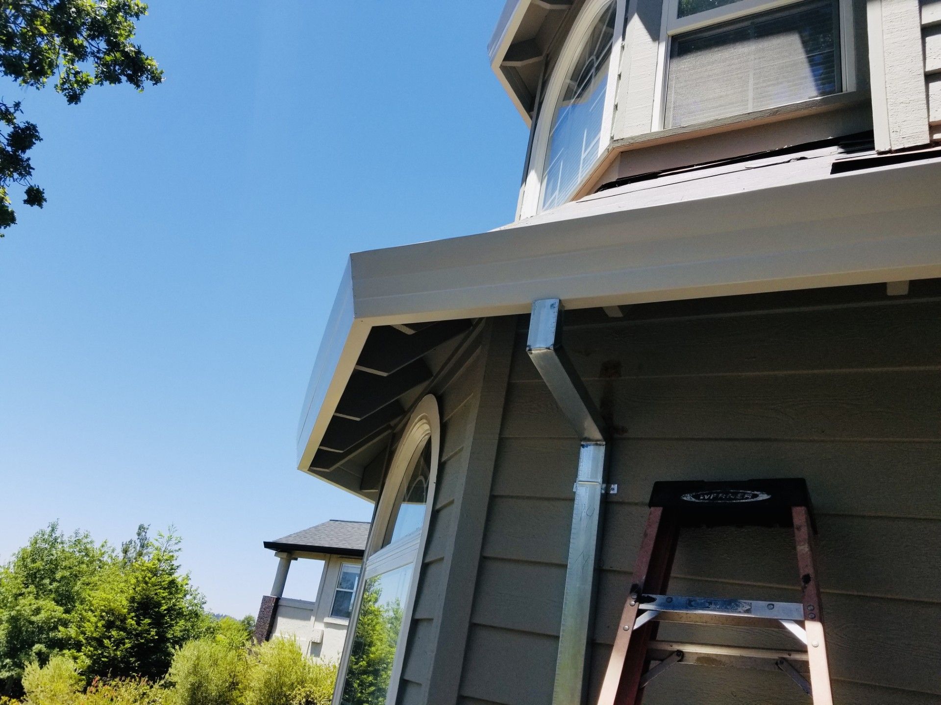 Exterior of a gray house with a ladder under the eaves against a blue sky