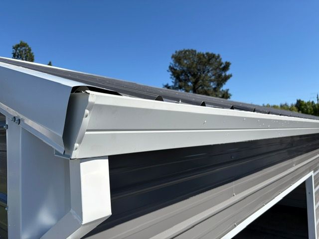 Close-up of a white roof gutter and fascia under a blue sky.