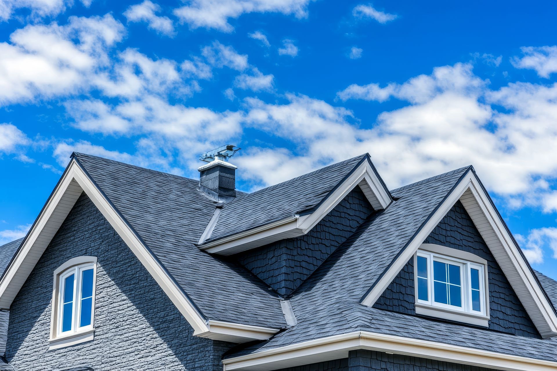 Residential Gutter Contractor view of a gray shingle roof with dormer windows and a chimney Residential Gutter Contractor view of a gray shingle roof with dormer windows and a chimney