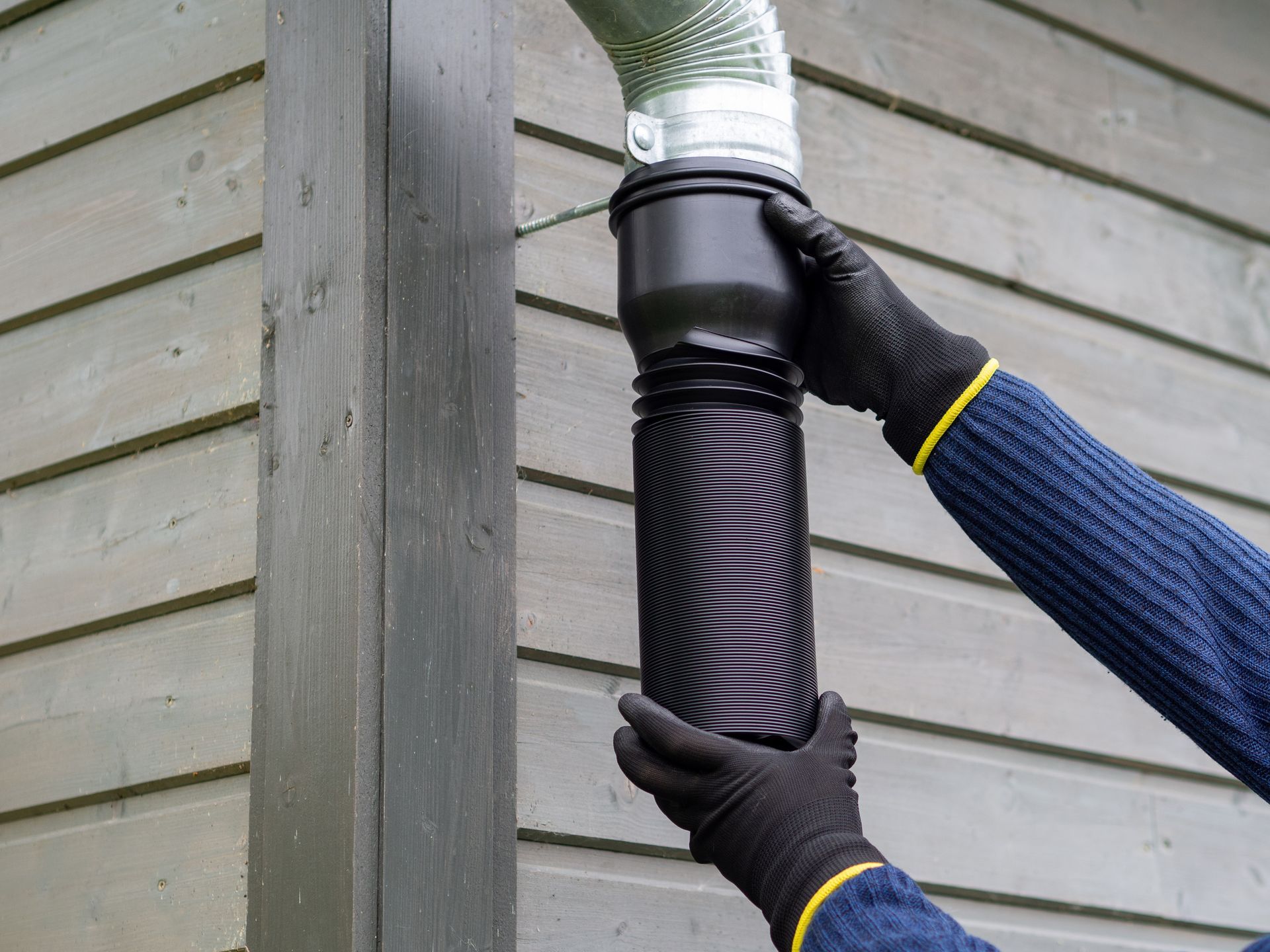 Gloved hands install a black downspout extension on a house gutter