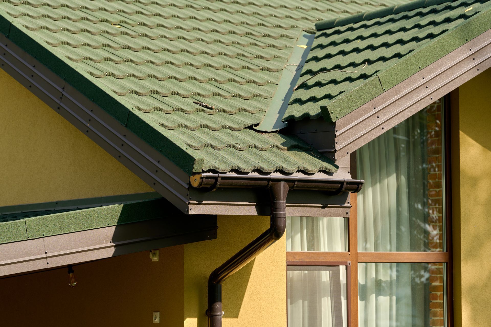 Green tiled roof and gutter on a yellow house with a window beneath.