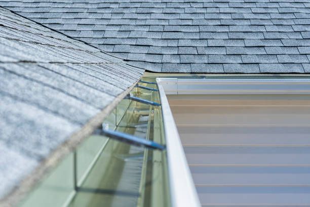 Roof edge with glass gutter and blue skylight panels under gray shingles