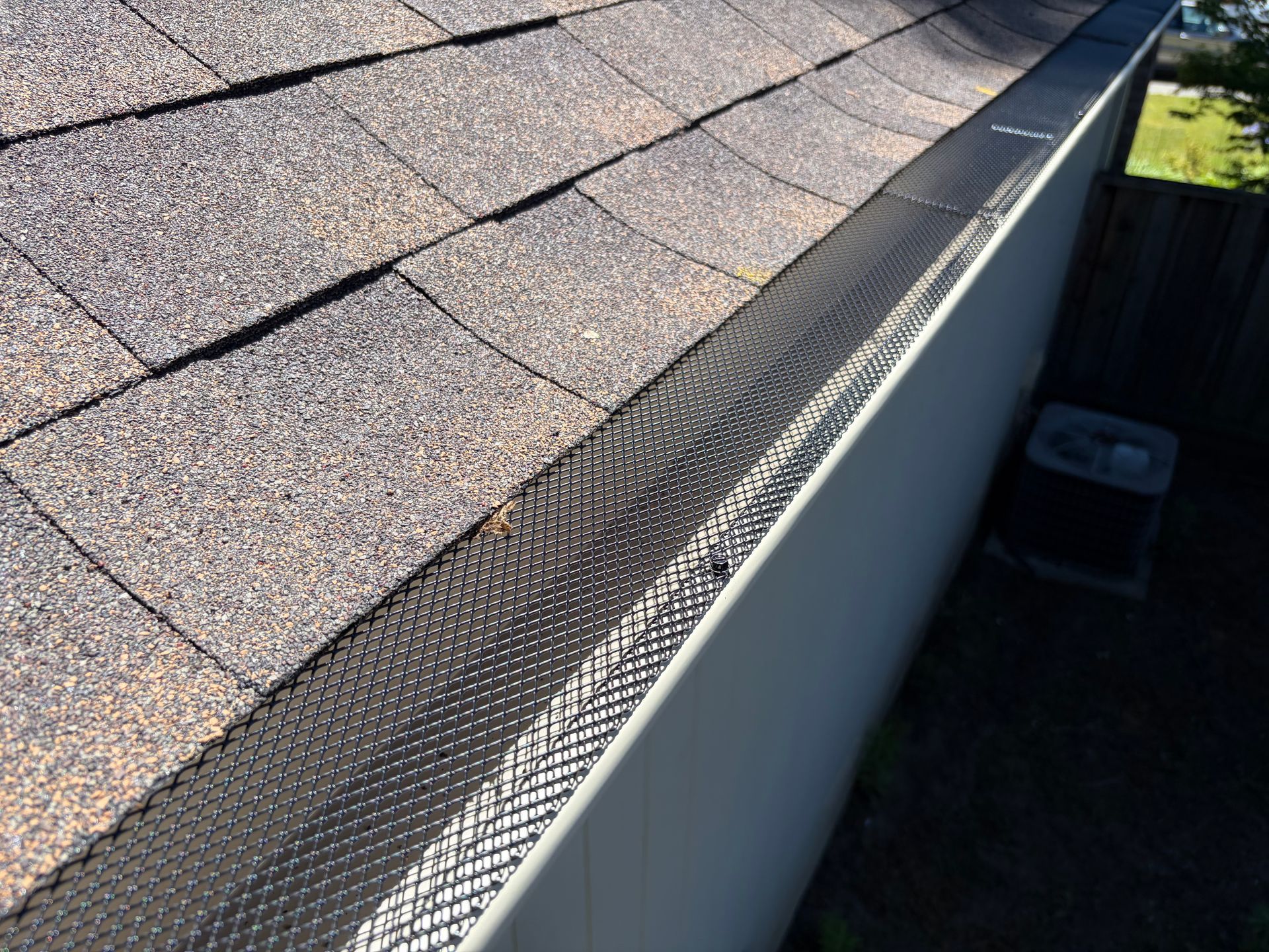 Close-up of a shingled roof edge with metal gutter guard and white fascia board Close-up of a shingled roof edge with metal gutter guard and white fascia board