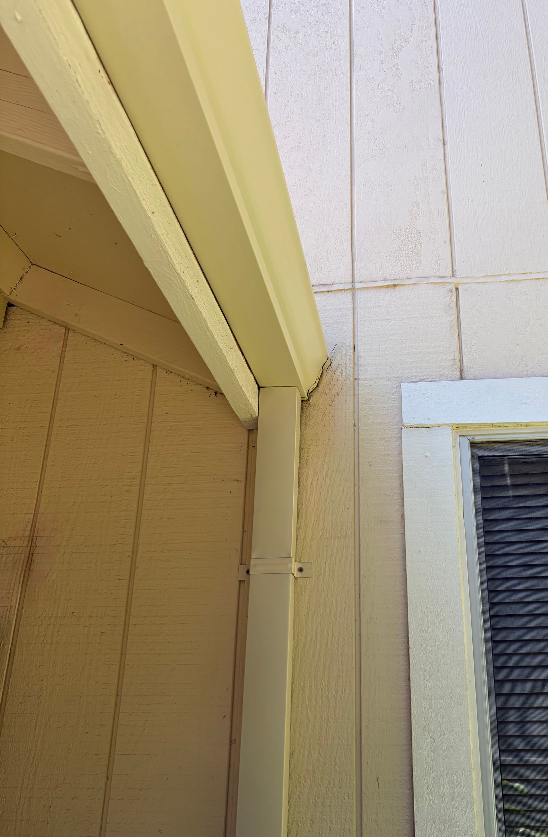 White seamless gutter and downspout installed along the exterior corner of a residential home.