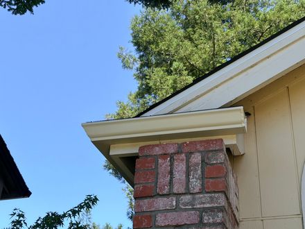 White seamless rain gutter installed above a brick column on a residential roof.