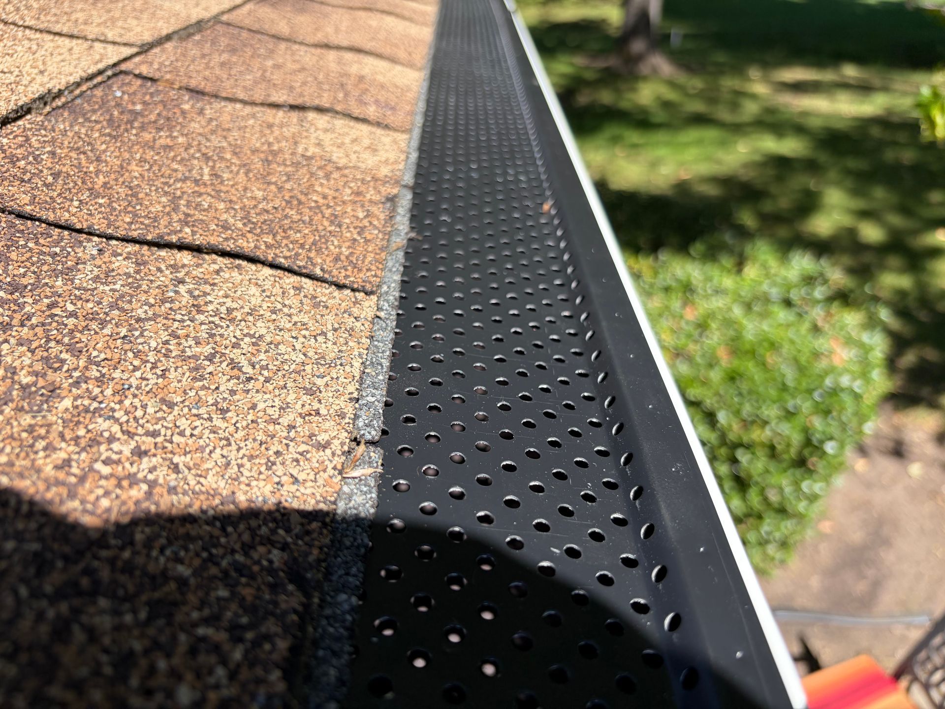 Black gutter guard installed over a white seamless rain gutter on an asphalt shingle roof.
