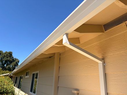 White aluminum rain gutter installed along the roof edge of a beige house exterior.