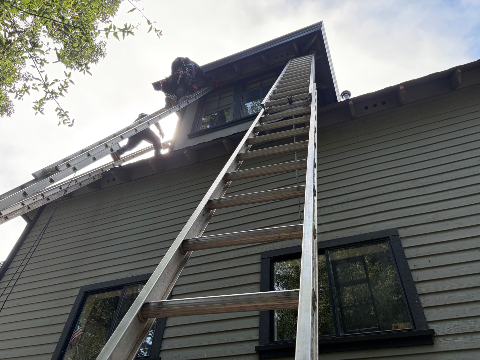 Roofing contractors on ladders performing roof repairs on a two-story home