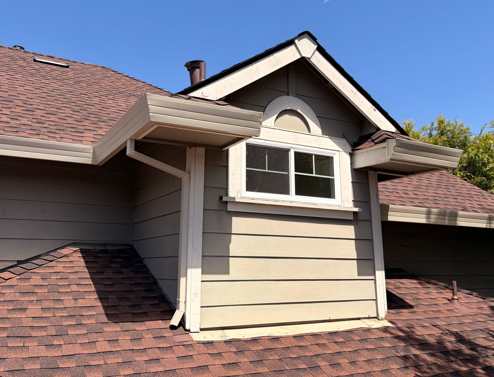 White seamless rain gutters installed on a residential roof with brown asphalt shingles.