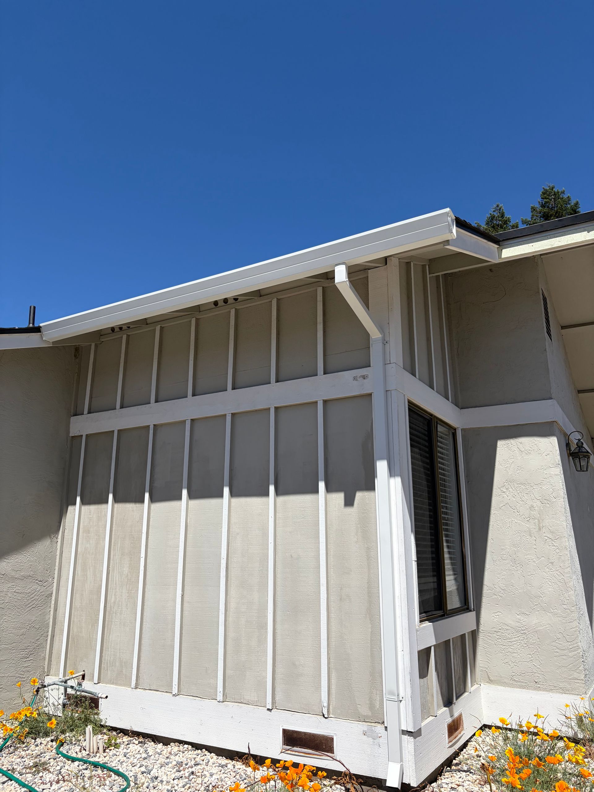 White seamless rain gutter and downspout installed on the exterior of a residential home.