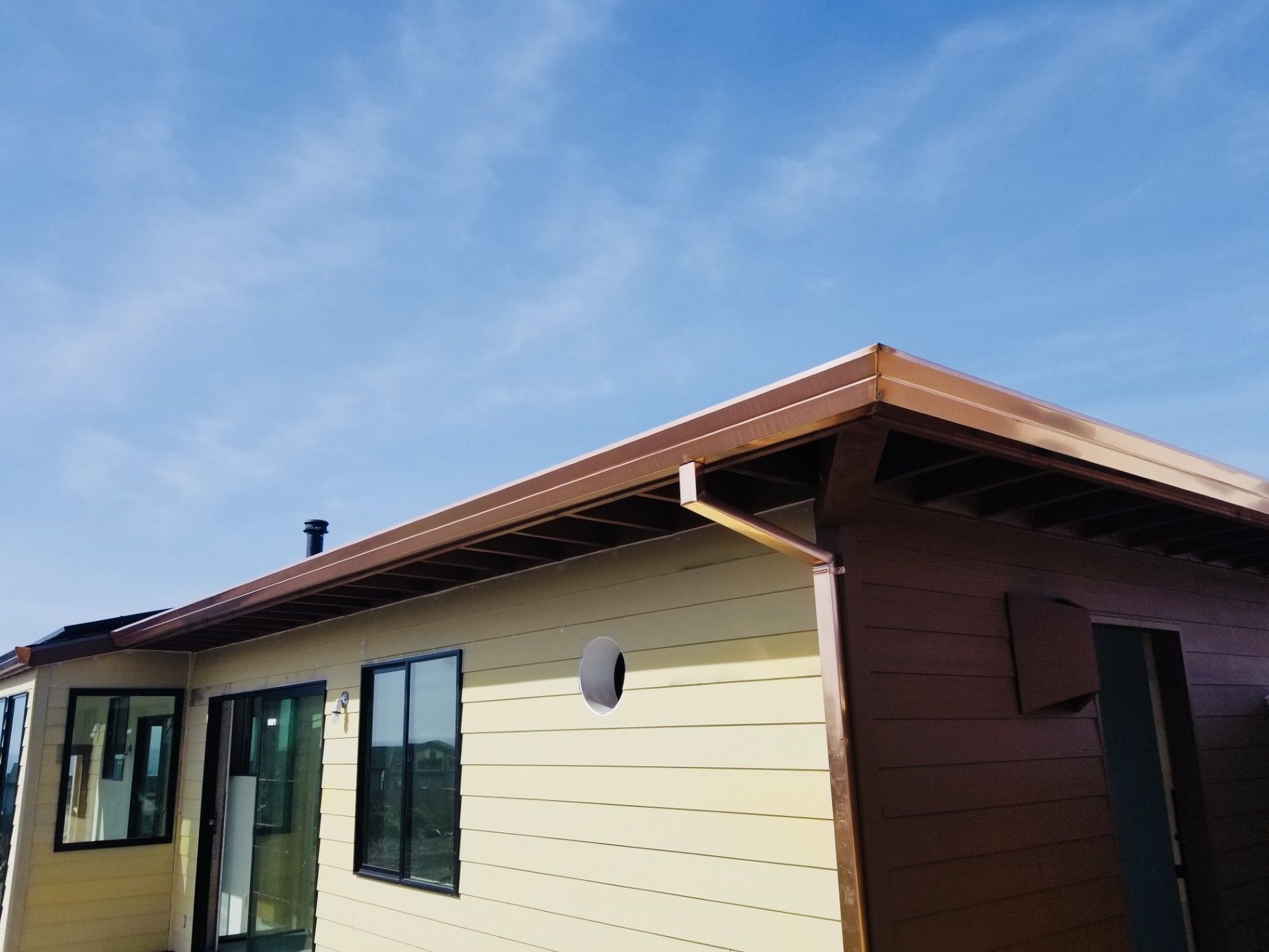 Single-story beige house exterior with dark brown roof and windows under a blue sky