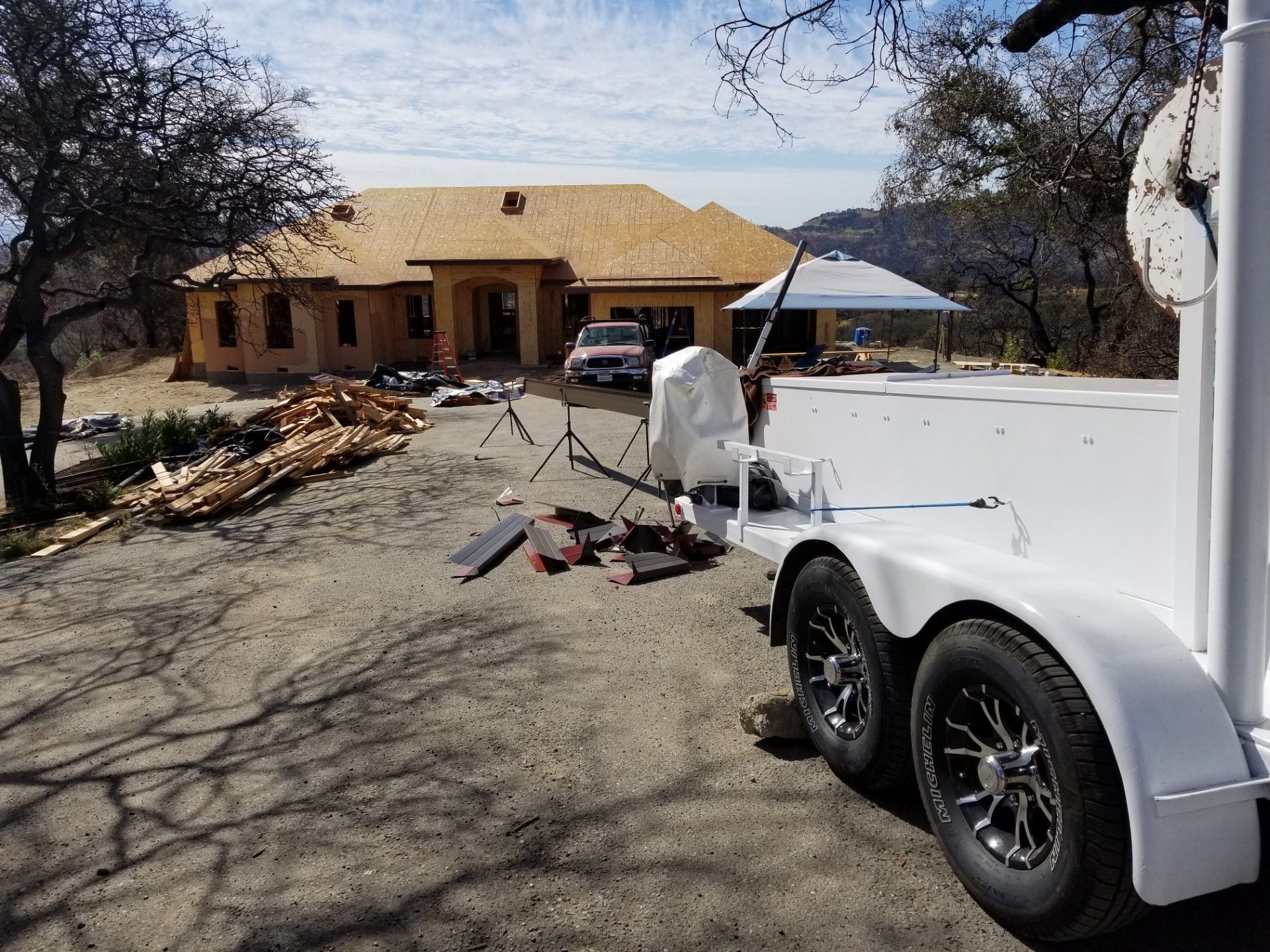 White trailer in driveway of a tan house with debris and a covered patio in the yard.