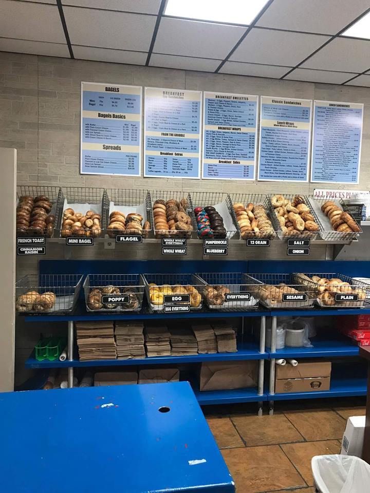 Bakery display shelves with assorted breads and pastries beneath blue menu signs in a shop.