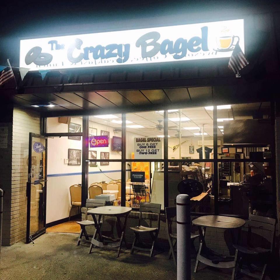 The Crazy Bagel storefront at night with outdoor tables and chairs under a lit sign.