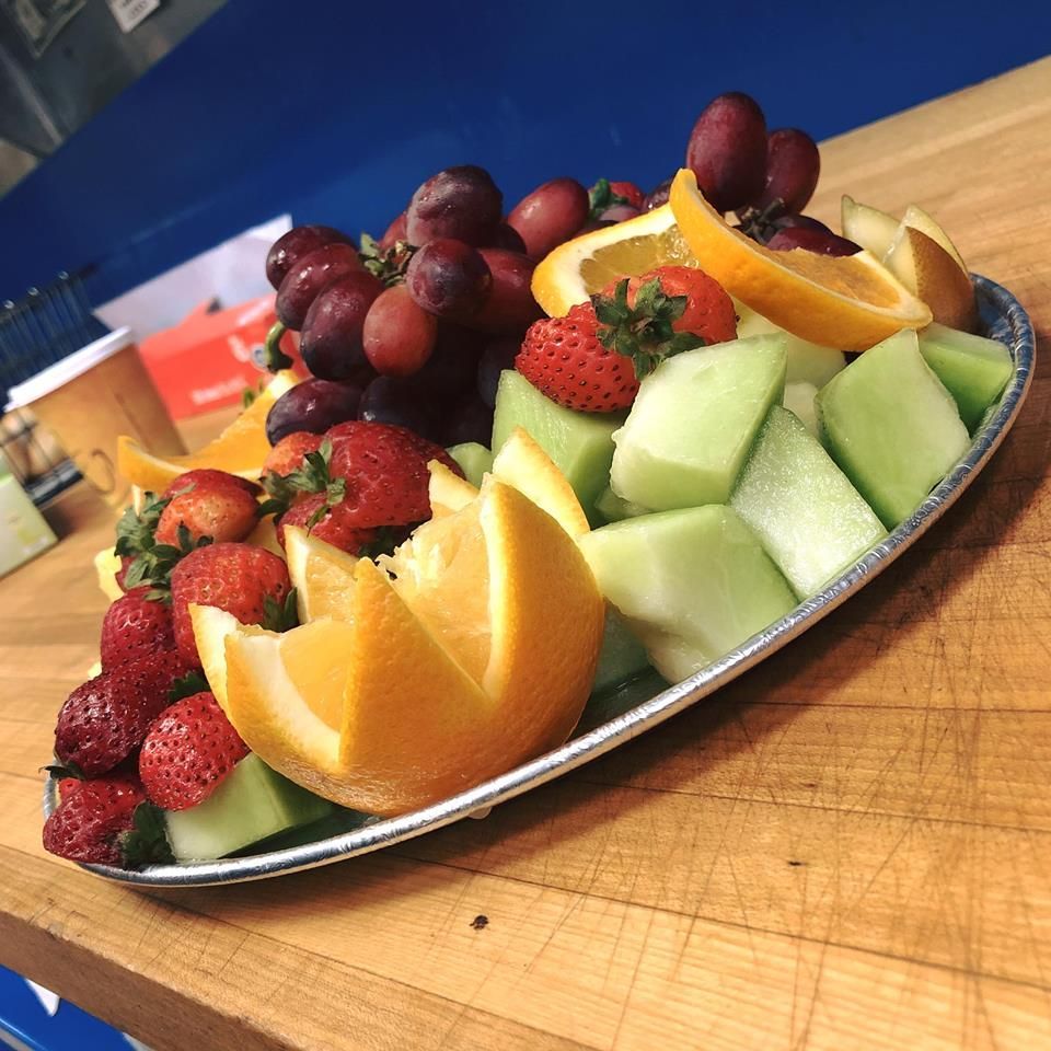 Tray of assorted fruit slices and berries, including strawberries, orange wedges, grapes, and melon on a wooden table