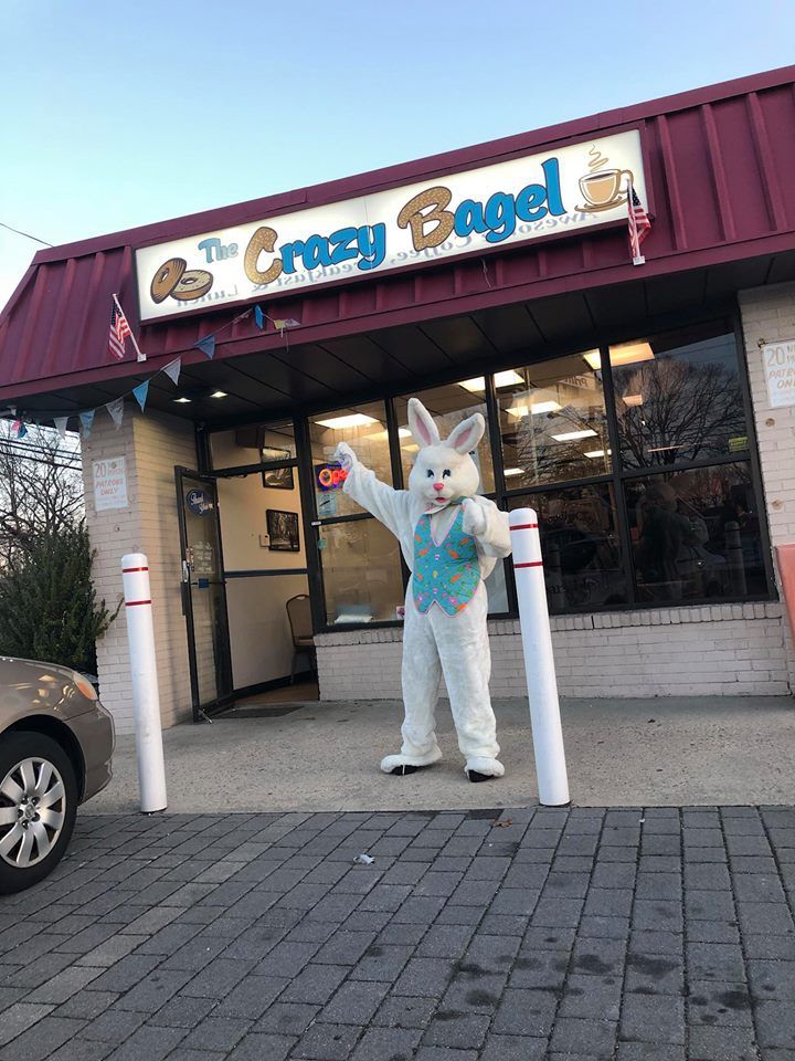 Person in a bunny costume standing outside The Crazy Bagel storefront.