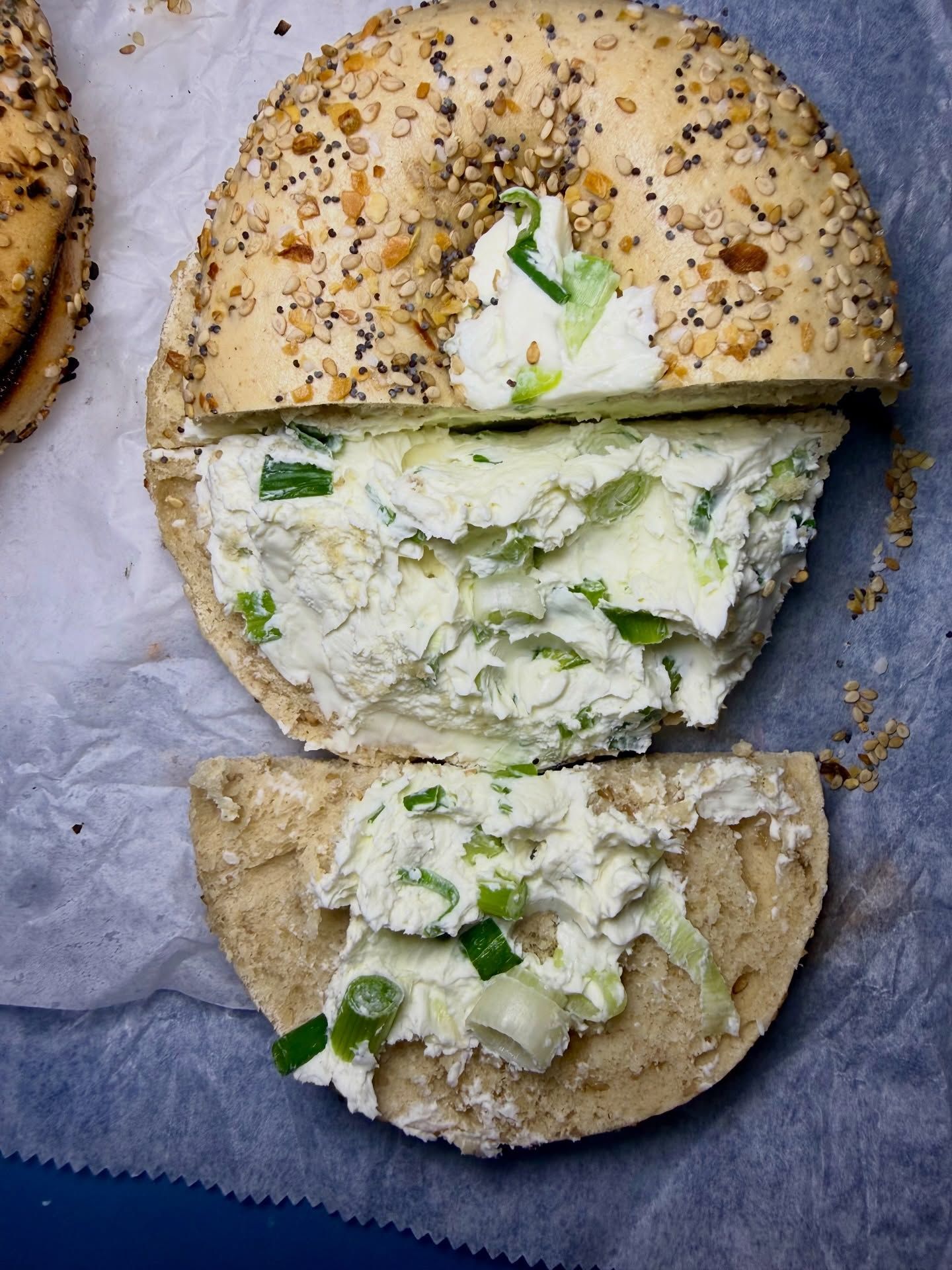 Everything bagel with cream cheese and green onions, partially sliced on parchment paper