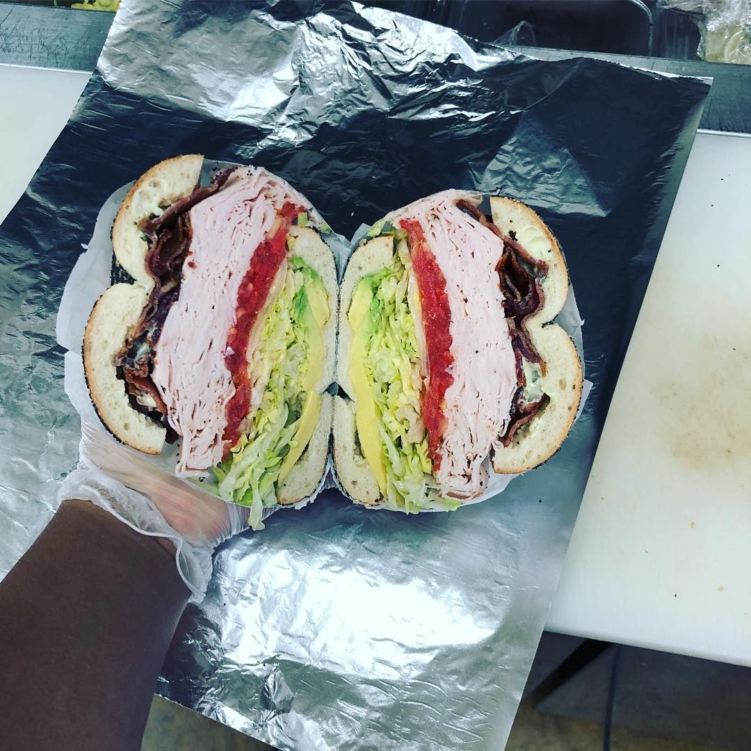 Large stuffed sandwich cut open, showing layers of meat, avocado, and condiments on foil wrap
