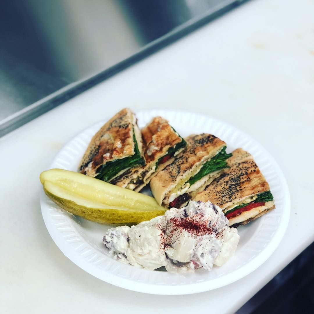 Grilled sandwich halves with pickles and potato salad on a white plate