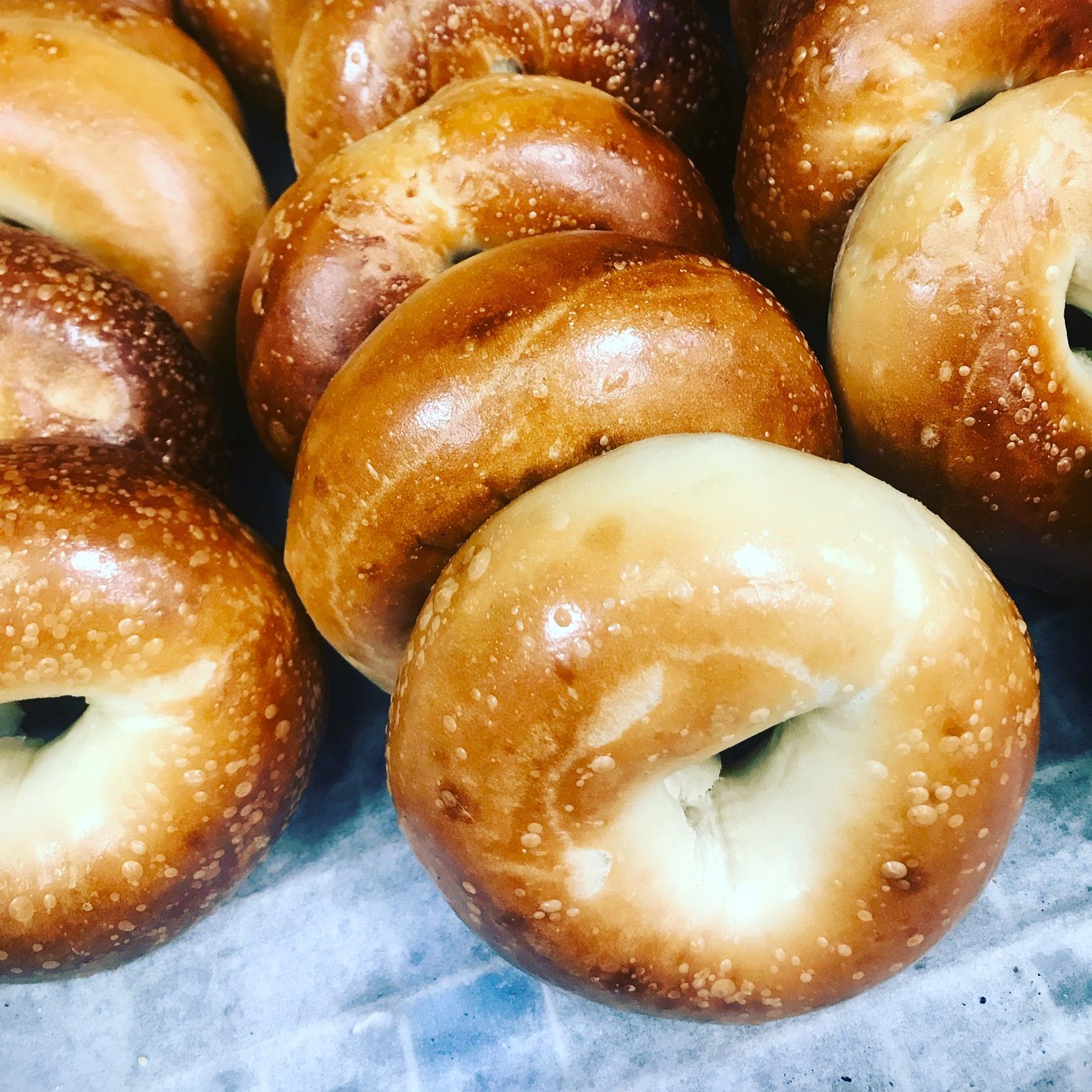 Assorted golden-brown glazed bagels stacked on parchment paper