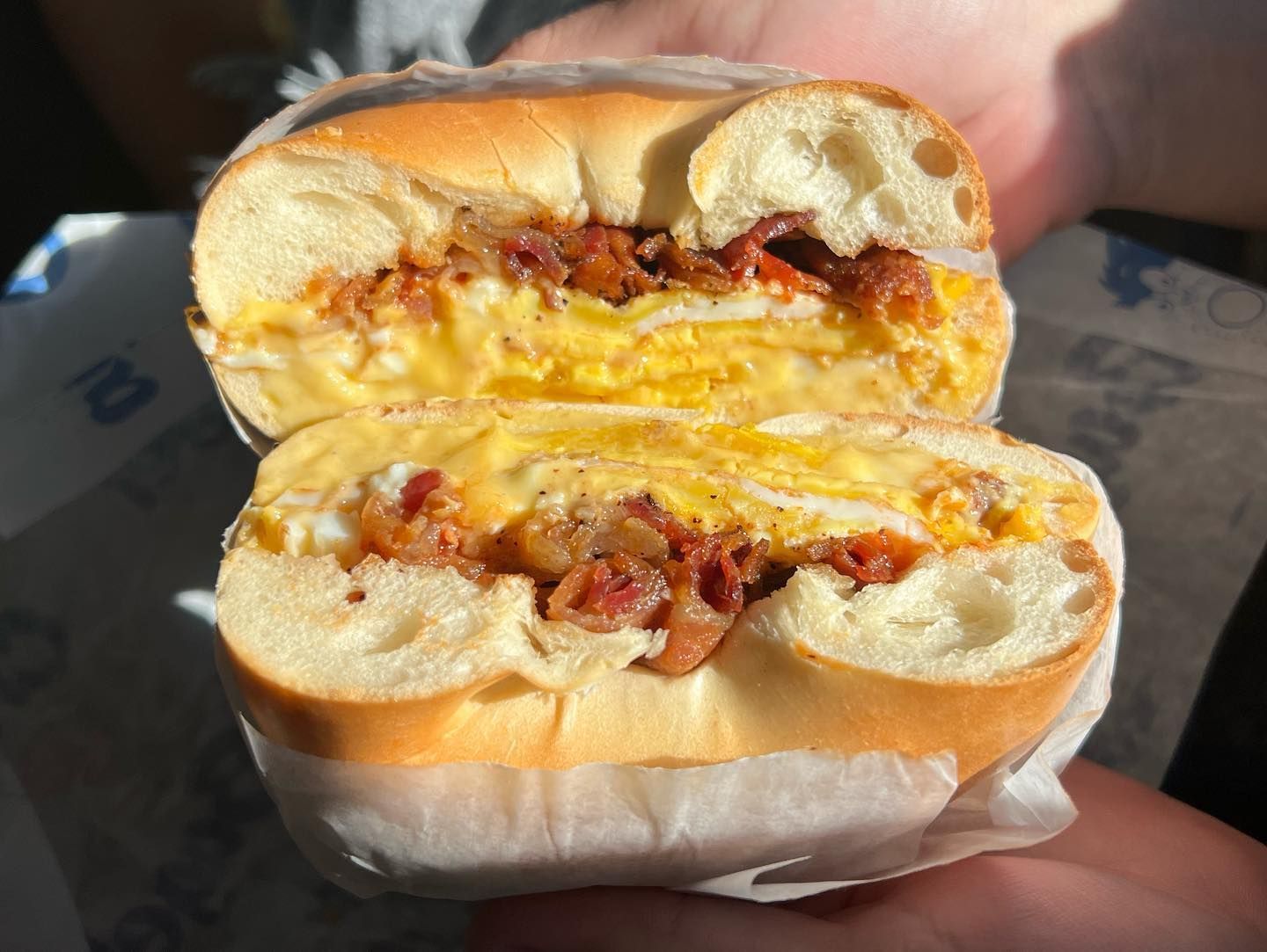 Cut sandwich with egg, bacon, and melted cheese held in a hand