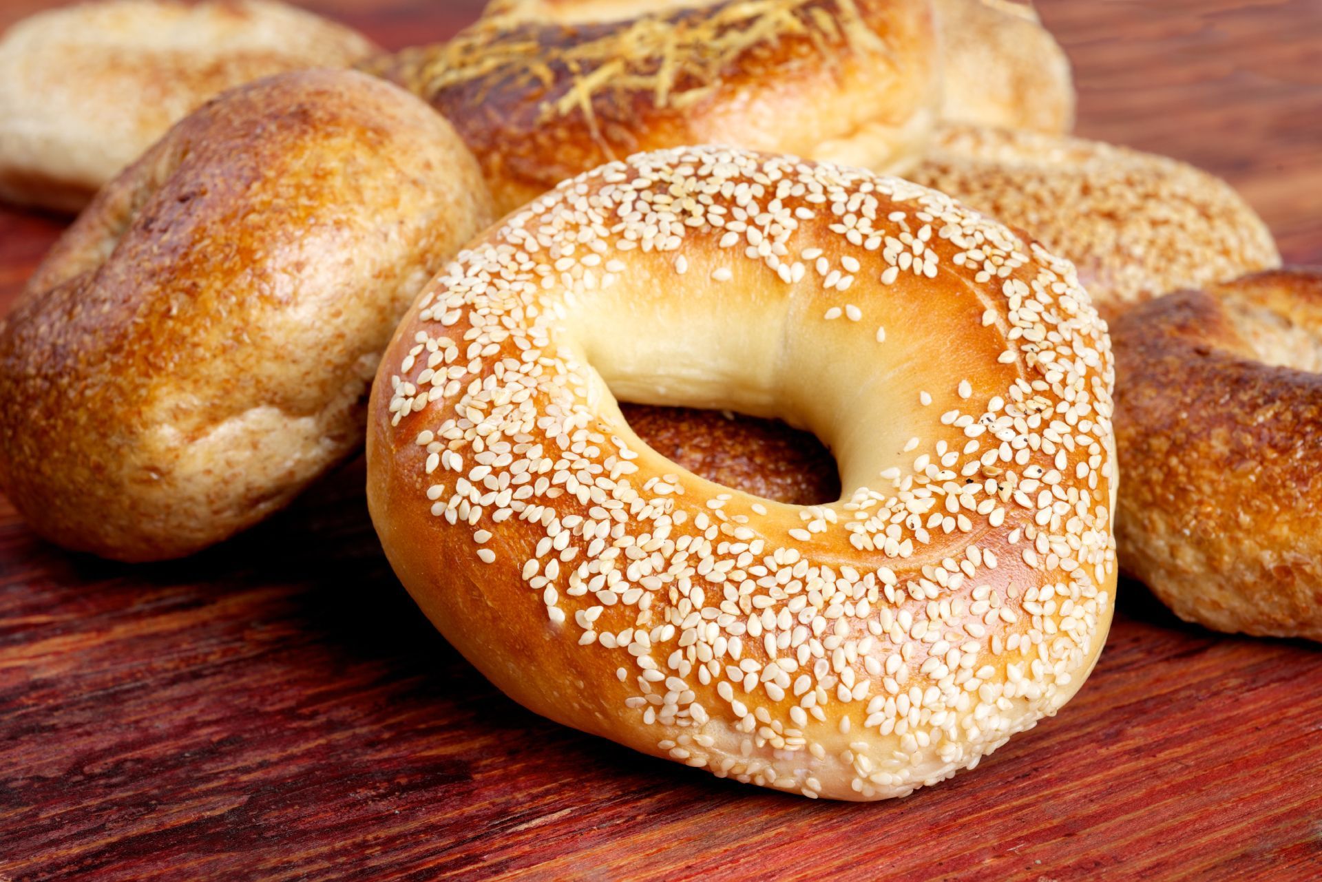 Assorted bagels on a wooden surface, including a sesame-coated bagel in the foreground.