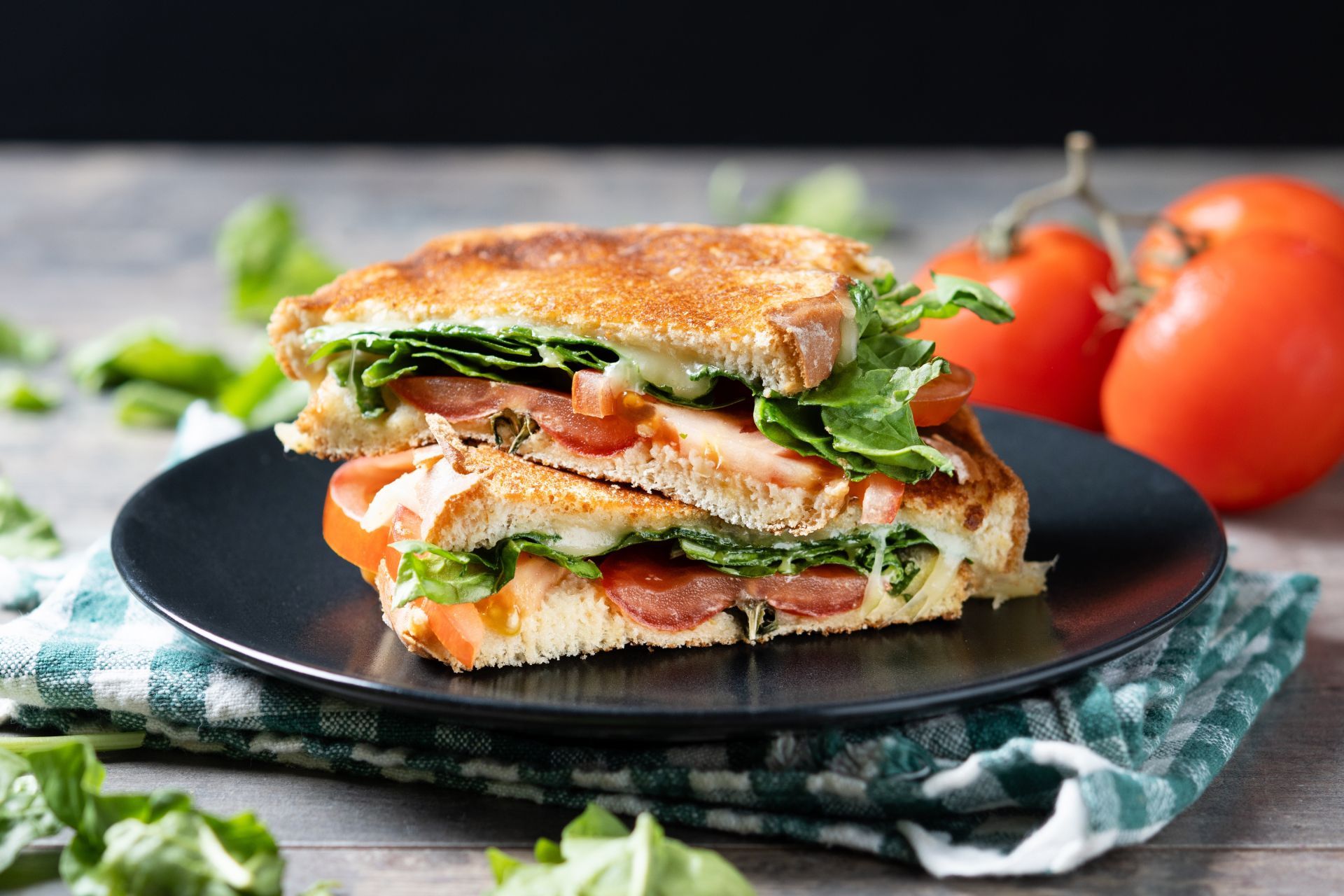 Stacked salmon and lettuce sandwich on a black plate with tomatoes in the background