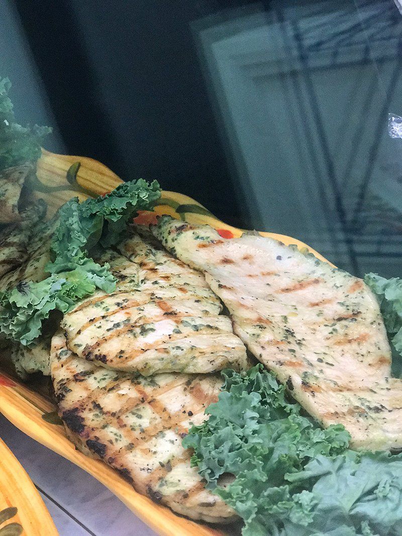 Grilled chicken breasts on a platter with greens and lemon wedges