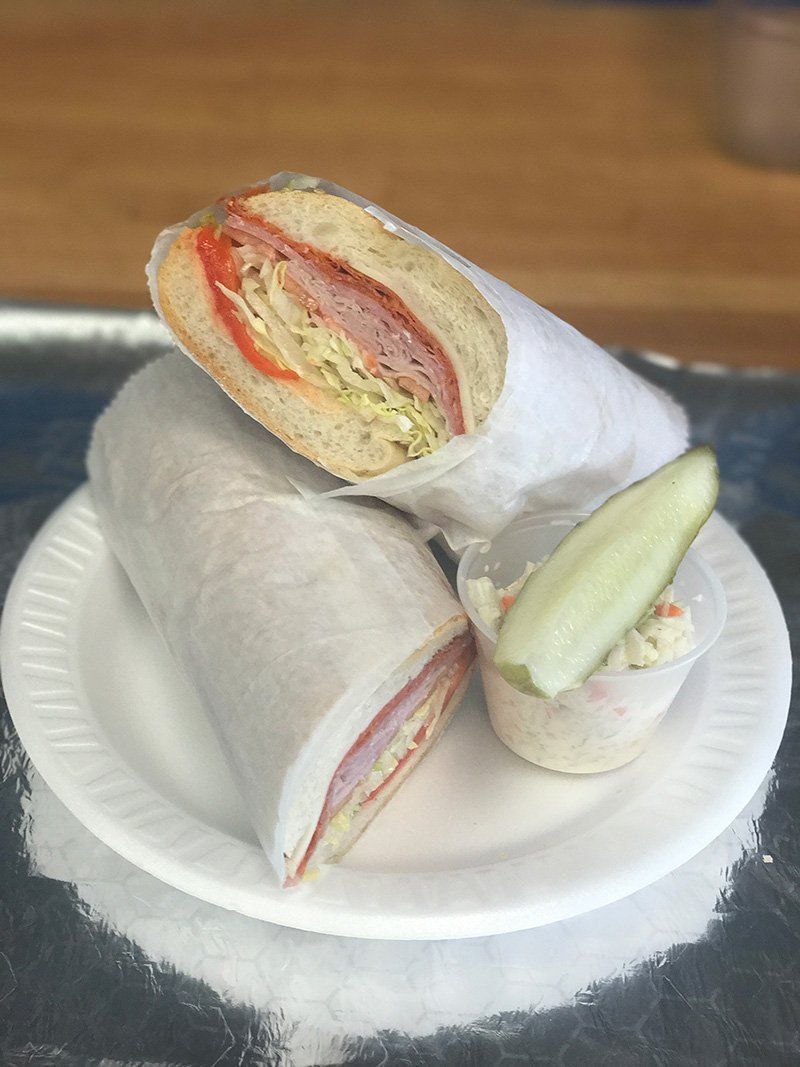 Three small sandwich halves on a white paper plate, wrapped in napkins on a wooden table.