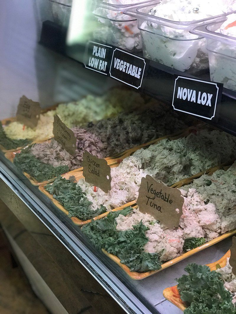 Bakery display case with assorted cakes, labeled with signs like “Nova Lux” and “Xang.”
