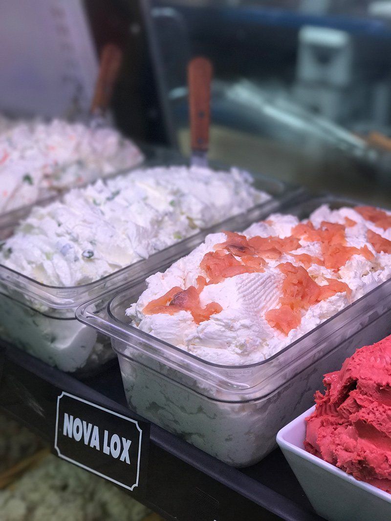 Trays of colorful shaved ice or dessert topping in a display case, with white, orange, and pink toppings