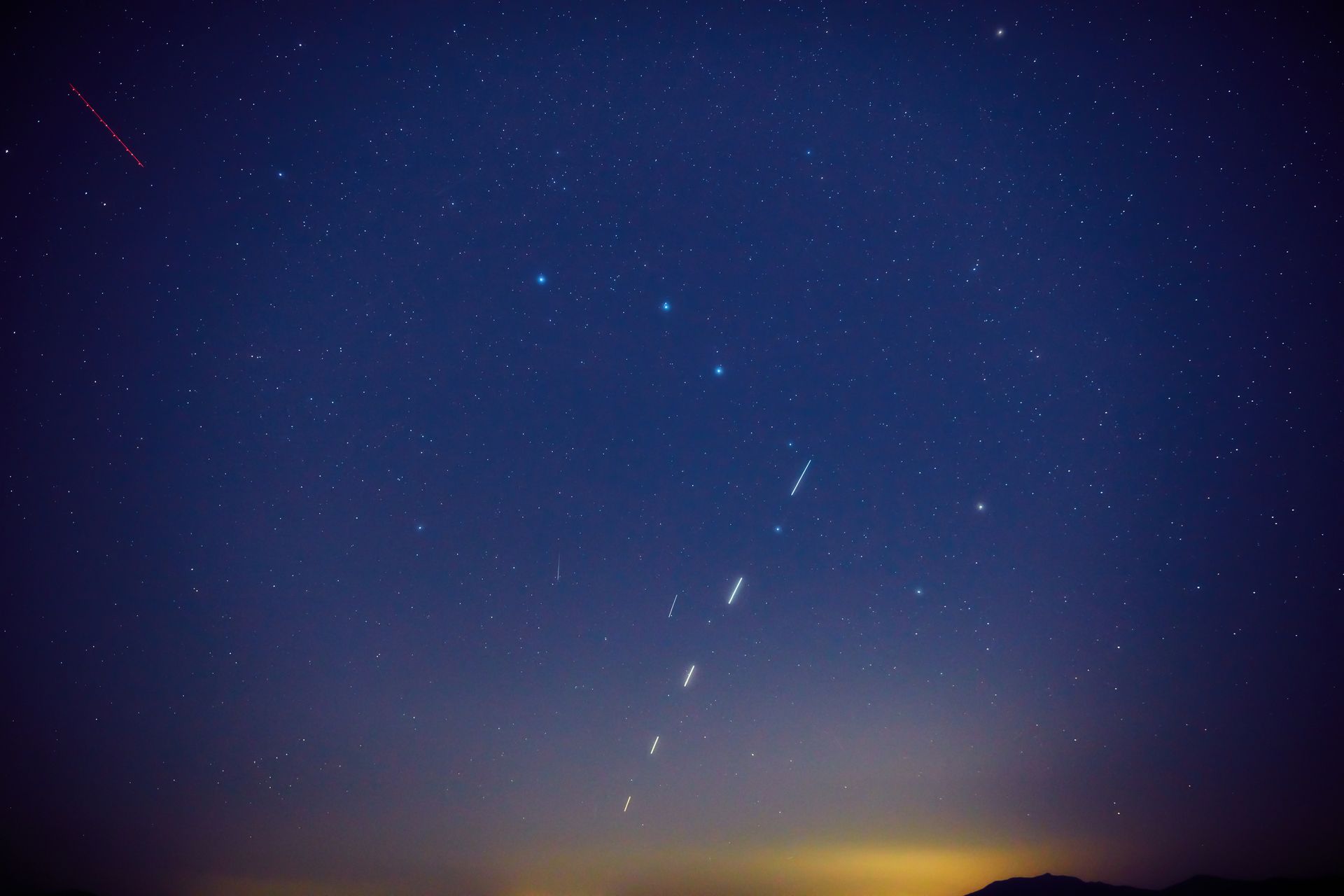 Starry night sky with a bright meteor streak above a glowing horizon
