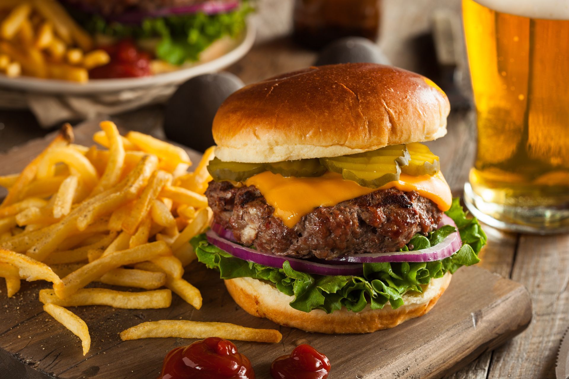 Cheeseburger with fries on a wooden board, with a pint of beer in the background