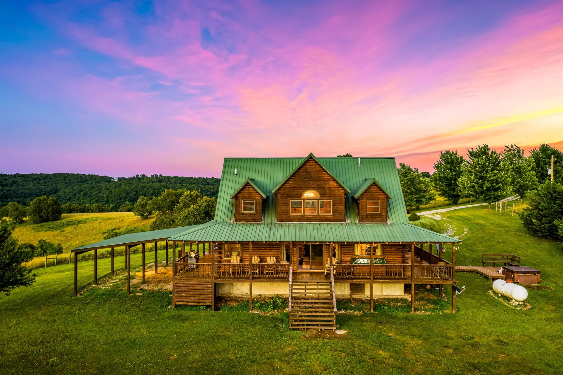 Rustic green-roof cabin on a grassy hill at sunset with a colorful pink and purple sky