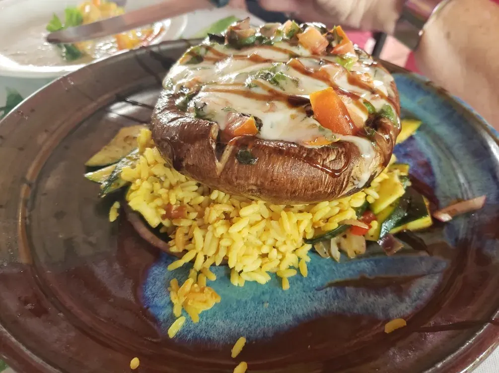 Grilled mushroom on yellow rice, drizzled with sauce, served on a dark plate.