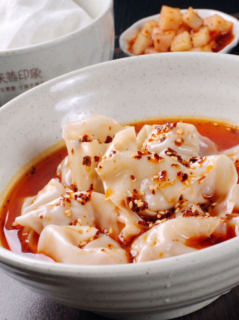 Black bowl of creamy soup topped with herbs and red peppers on a wooden table