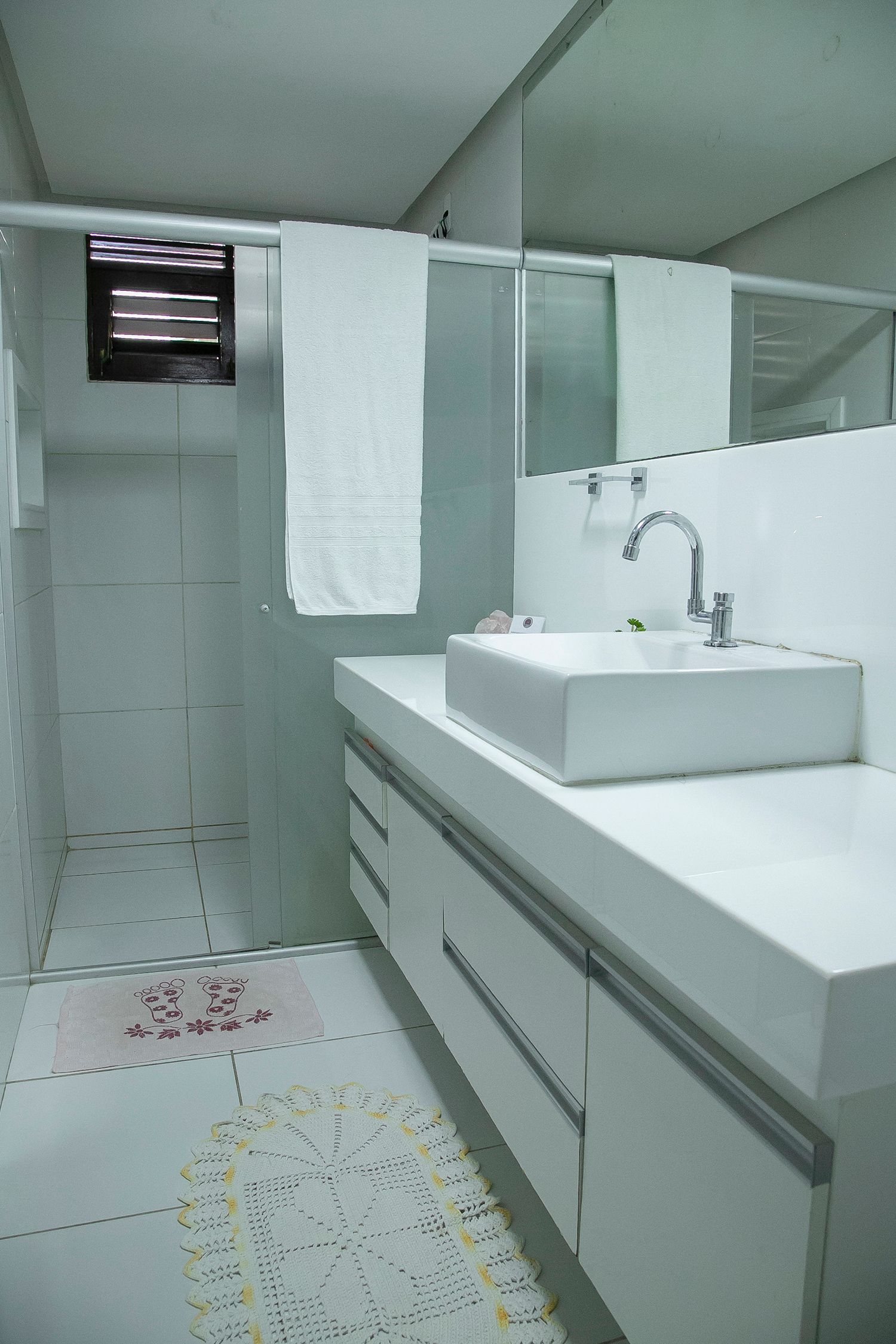 Banheiro branco com pia, espelho, toalha e paredes e piso revestidos com azulejos.