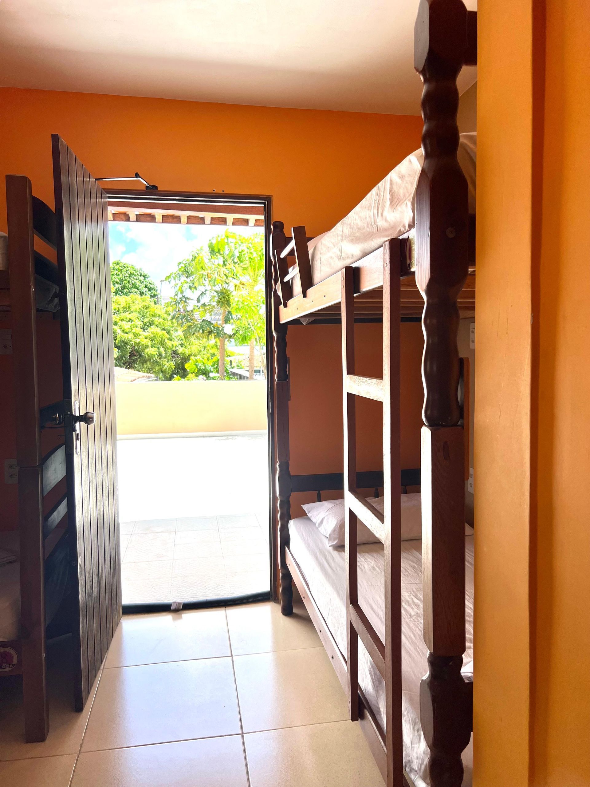 Quarto estreito com beliches que dá para uma porta aberta e uma vista externa iluminada.