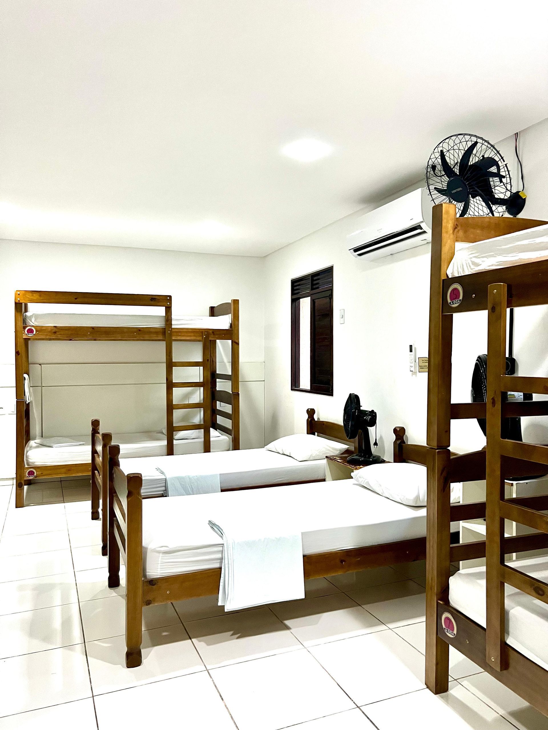 Quarto de dormitório com beliches de madeira, camas de solteiro e ar-condicionado de parede.