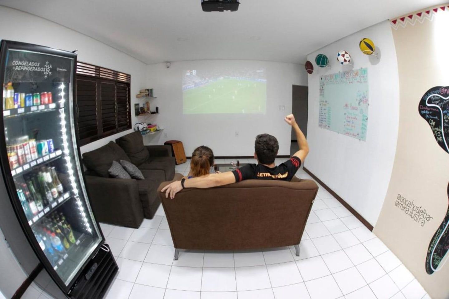 Duas pessoas sentadas em um sofá assistindo a um filme projetado em uma sala de estar.